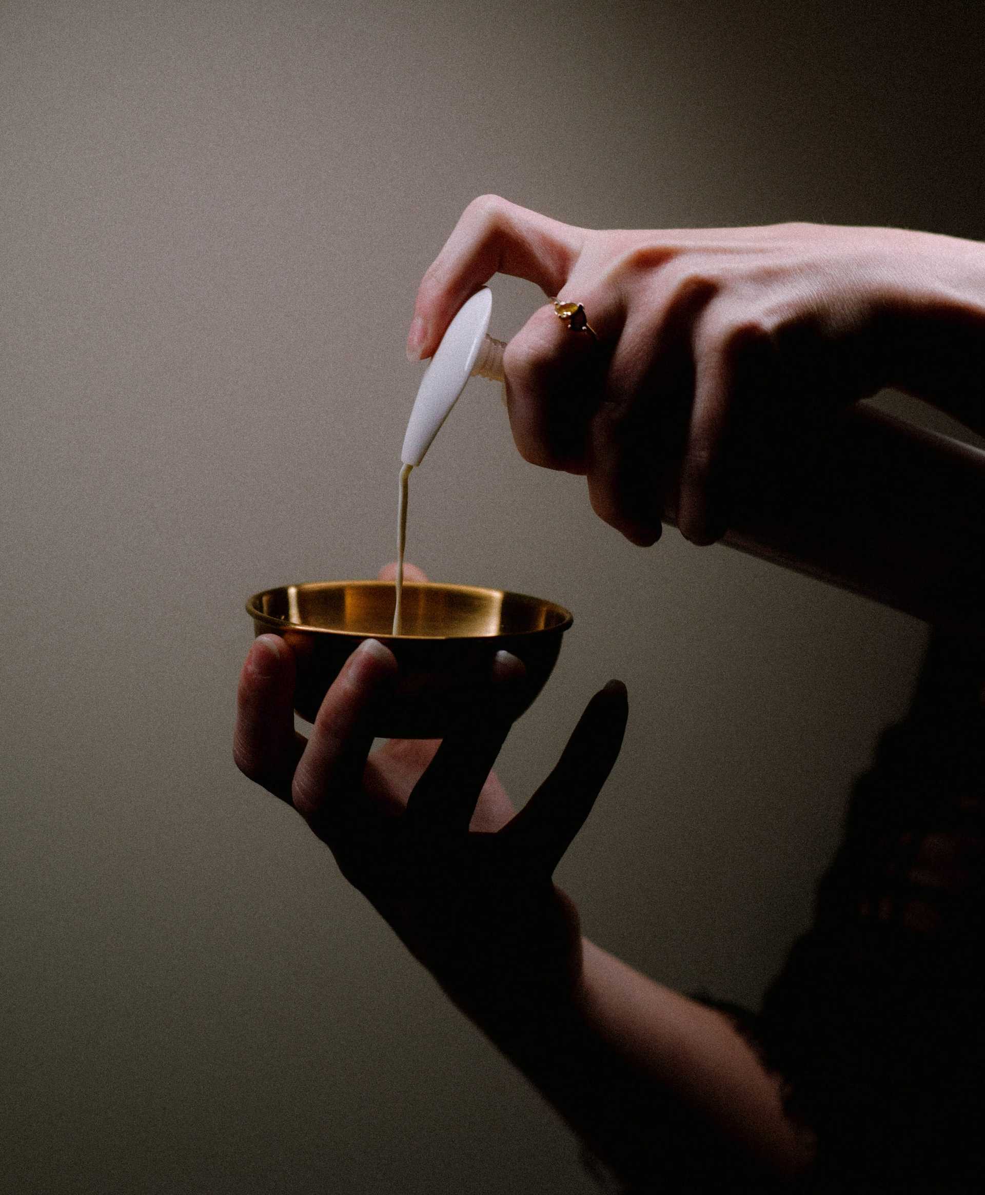 Pouring oil into a golden bowl held by a person's hand.